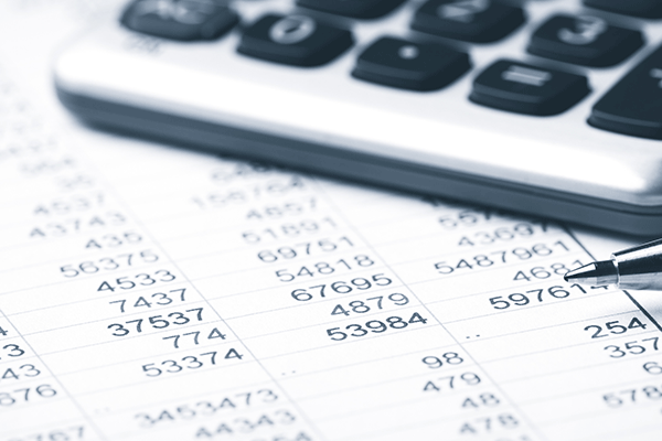 A black and white picture of the corner of a calculator and the tip of a pen on a piece of paper with multiple numbers in list format.