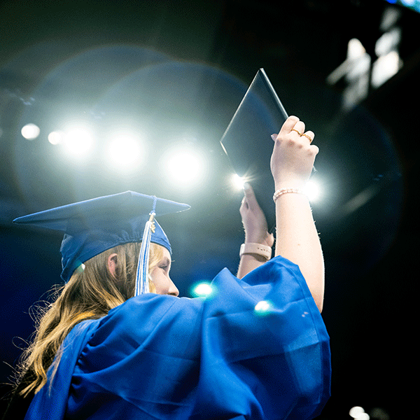 A student in a cap and gown holds up a diploma book