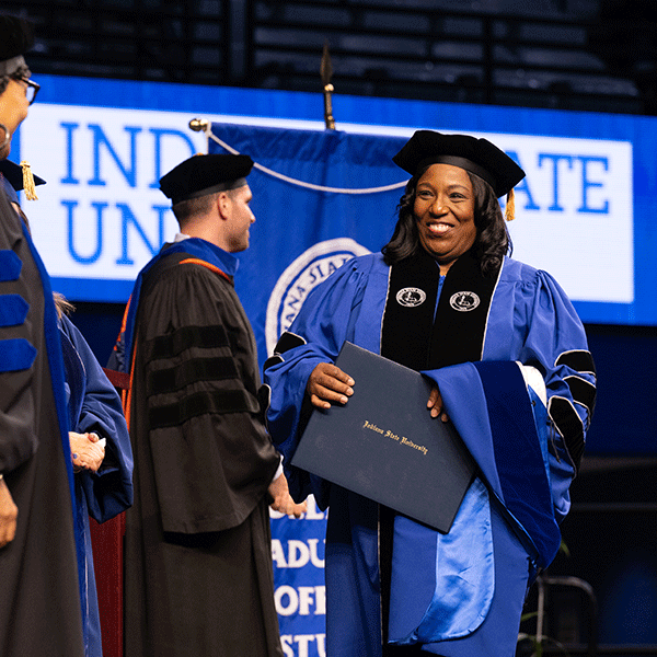 A woman smiling as she walks across the stage with her diploma in hand.