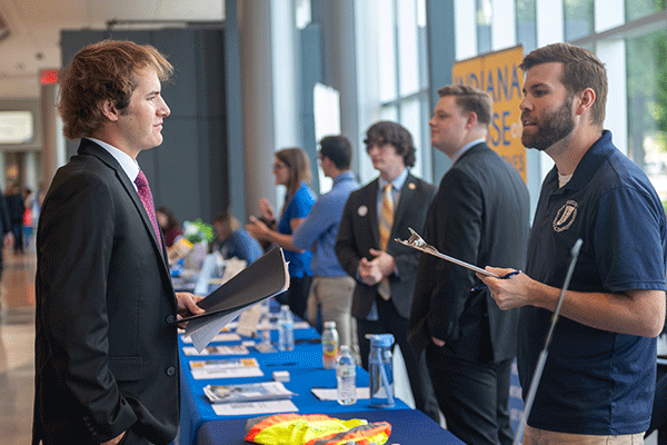A photo of two men talking to one another at a job fair.