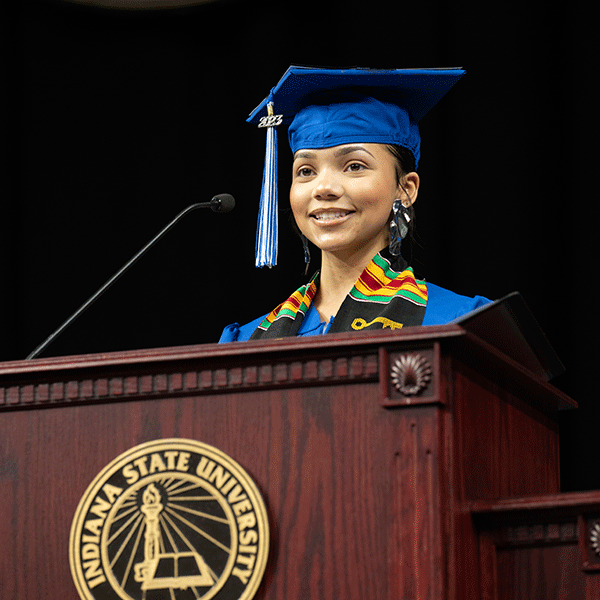 A student in a cap and gown stands at the podium on the Commencement stage