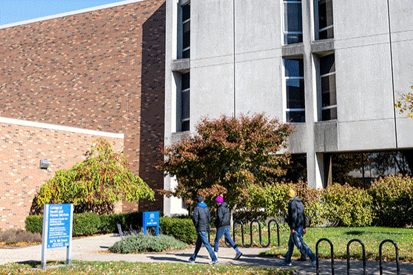 Three students walk past the front of the ISU Health Center building on a summer day. 