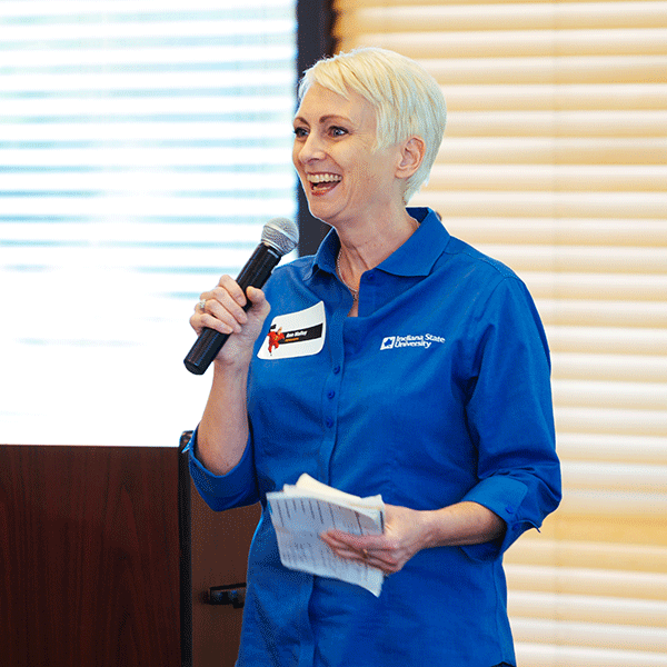 A middle aged employee wearing an Indiana State University shirt smiles while talking into a microphone during an Enrollment Management retreat for employees.