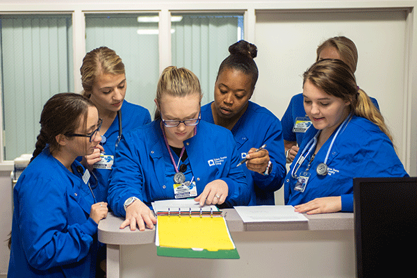 A group of six nursing students all look over a chart