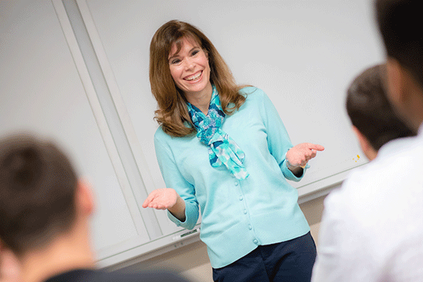 Emily Cannon, DNP, Associate Professor of Nursing, teaches a group of nursing students in one of the newly renovated classrooms for nursing students at Indiana State University. The smiling woman with brown hair is standing at the front of the classroom and is wearing a light blue blouse and dark slacks.