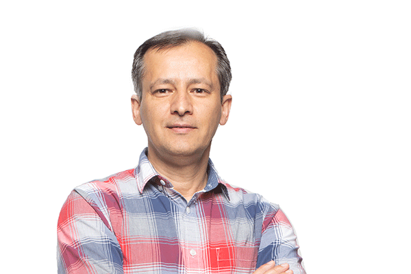 A middle-aged male of Middle Eastern descent is posing with his arms crossed. A white backdrop is behind him. He wears a red, blue, and grey flannel dress shirt.