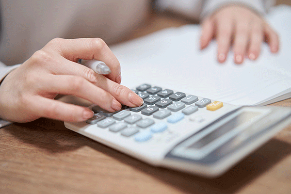 Hand typing on a calculator with papers on desk in background