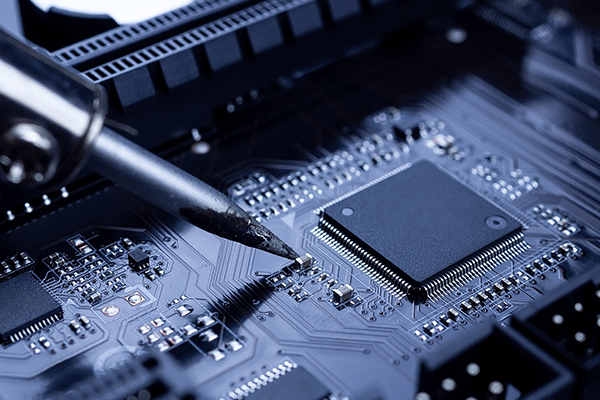 Close-up image of a dark grey computer chip in the panel of a computer, with a dark, pointed metal tool touching it. 