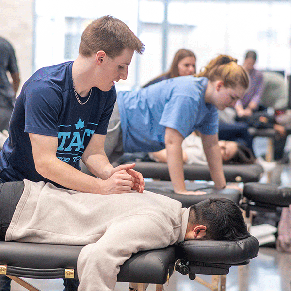 A massage therapy male student performs a massage in the hallway of the Health and Human Services building as part of a series of free sessions open to faculty, students and staff.