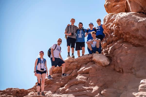A group of students stand and pose for a photo on a large rock in a Utah national park.