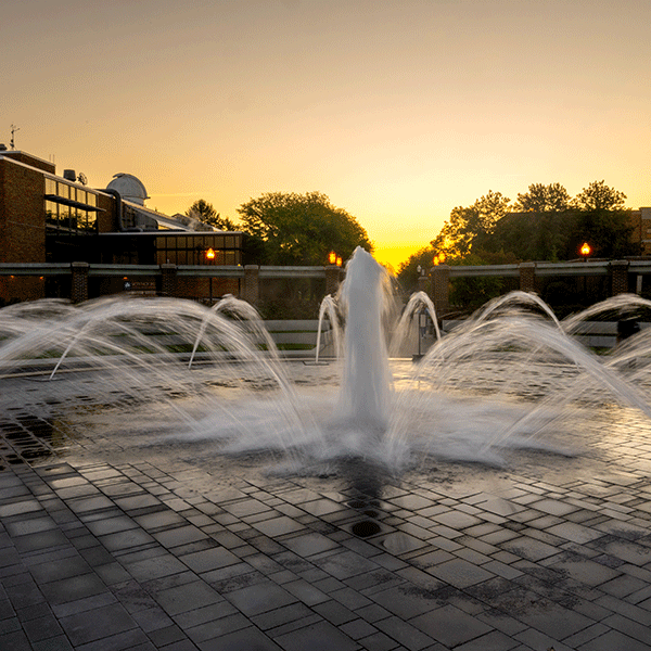 Evening photo of the Dede Plaza Fountain with sunset in the background.