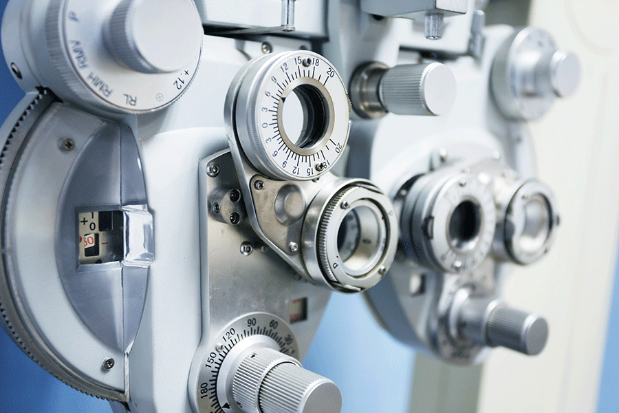 A close-up photo of optometry equipment, including an ultramatic RX master phoropter used for refraction of the eye. The machine is white and silver and has assorted dials and lenses.  