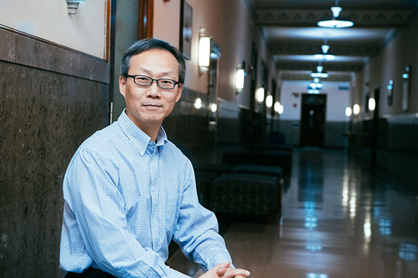 Male professor looking into the camera on the left side of the image with a hallway visible on the right.  