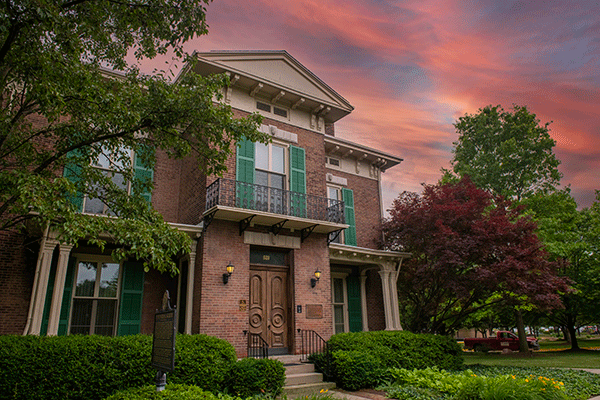  Exterior photo of a brick, two story building with steps leading to the front door in late evening with a  reddish sky and clouds.