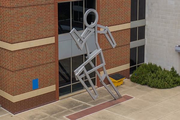 Aerial photo of a large building with a metal statue shaped as a runner in front of the structure.