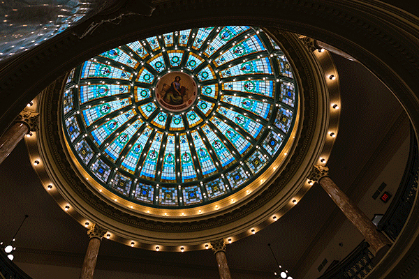 A large, colorful and intricate dome is illuminated in the ceiling of a large open space in Normal Hall.