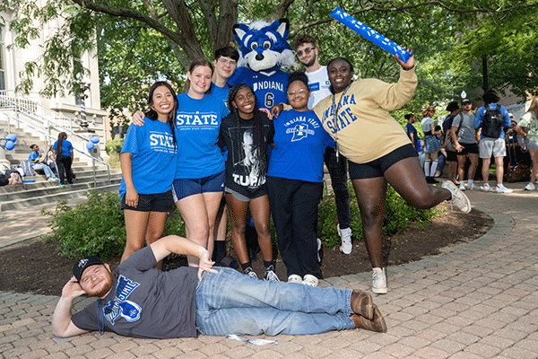 A diverse group of Sycamore students pose for a group photo with Sycamore Sam, the blue woodland creature and mascot of the university, in front of Normal Hall during an event in Fall. 