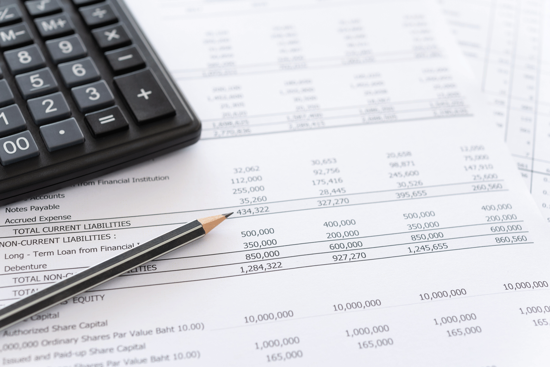 Detailed image of a white spreadsheet sitting on a table with a calculator in the top right corner of the frame.