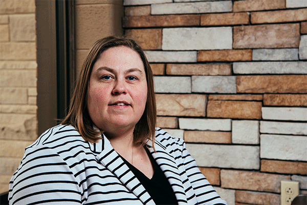 Middle-aged woman with shoulder-length brown hair looking at the camera wearing a white jacket with black stripes, and a black shirt. 