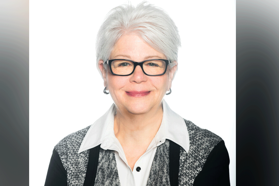 A photo of President Deborah J. Curtis, a white woman with short grey hair. She wears black glasses, and she looks straight ahead. She wears a grey-and-black shirt with a white shirt underneath. A grey border is around the photograph.