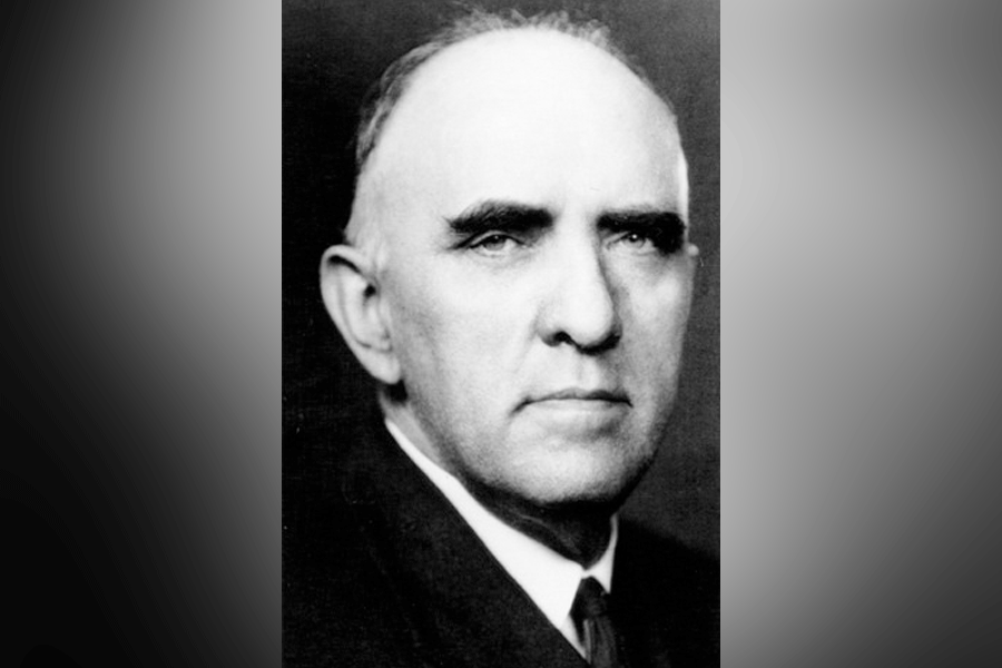  A black-and-white photograph of a man (President Linnaeus Neal Hines) with short hair. He looks straight ahead. He wears a suit, a white shirt, and a tie. A grey border is around the photograph. 