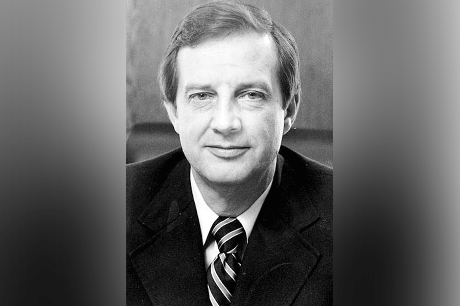 A black-and-white photograph of a man (President Richard George Landini) with short hair. He looks straight ahead. He wears a suit with a white shirt and a striped tie. A grey border is around the photograph. 