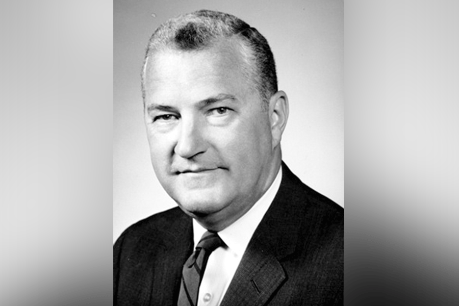 A black-and-white photograph of a man (President Alan Carson Rankin) with short hair. He looks straight ahead. He wears a suit with a white shirt and tie. A grey border is around the photograph. 