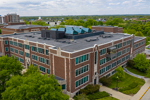 Aerial image of a large, square, brick three-story building in summer