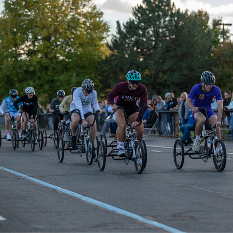 A group of participants race on tricycles in the Trike Derby at Indiana State University, with spectators watching from the sidelines.