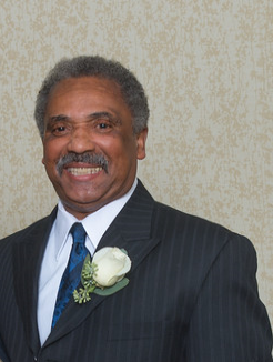 Portrait of Charlie Brown, an elder African American man smiling, wearing a dark suit with a white rose boutonniere.