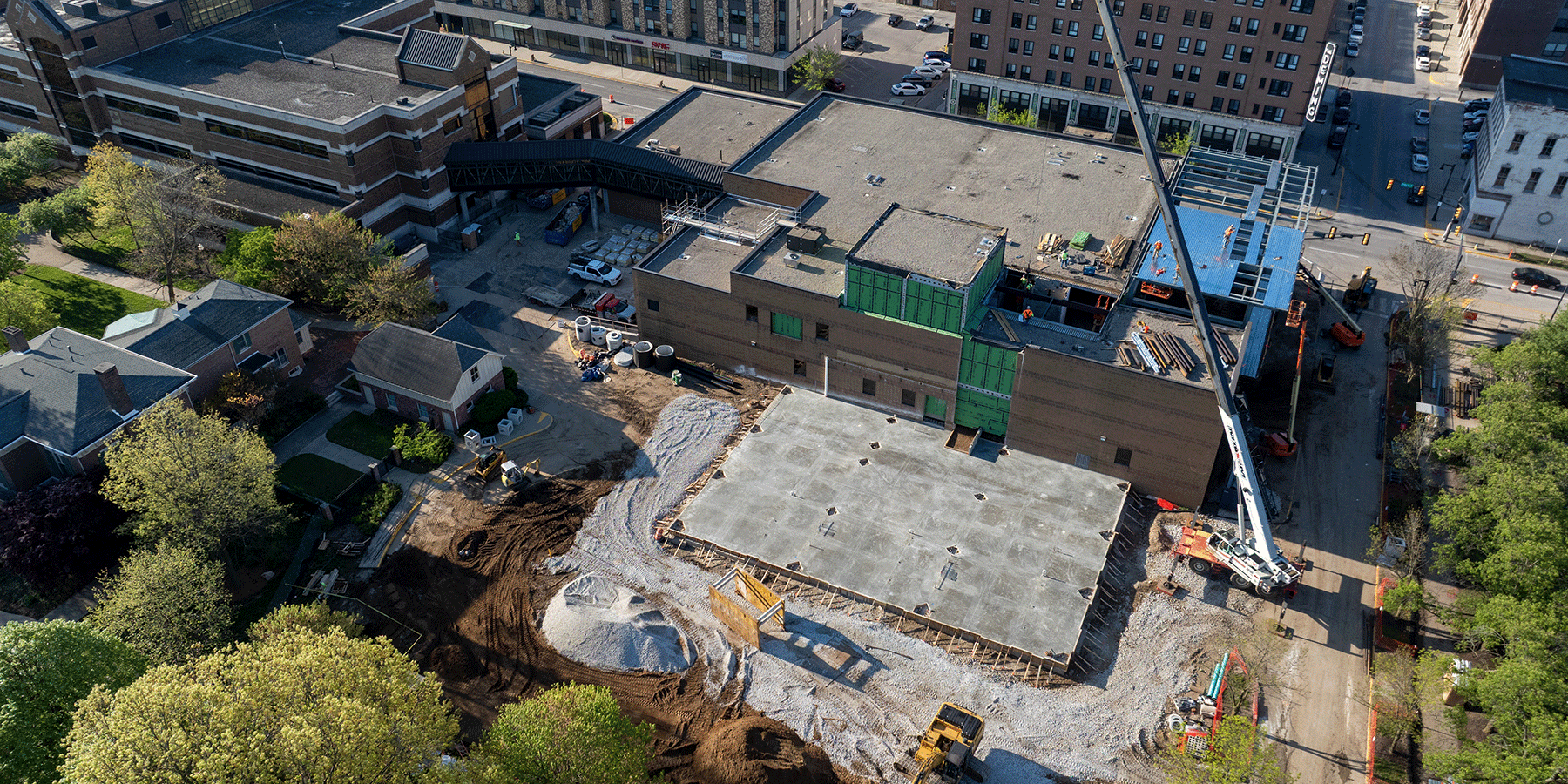 Aerial view of a construction site with a concrete foundation, crane, and equipment next to a large brick building.