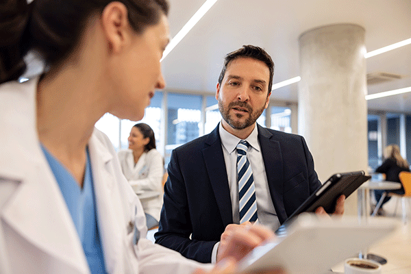 Professional in a suit holding a tablet speaks with healthcare staff in a modern office setting.