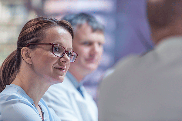 Healthcare professional wearing glasses listens attentively during a discussion with colleagues in a clinical setting.
