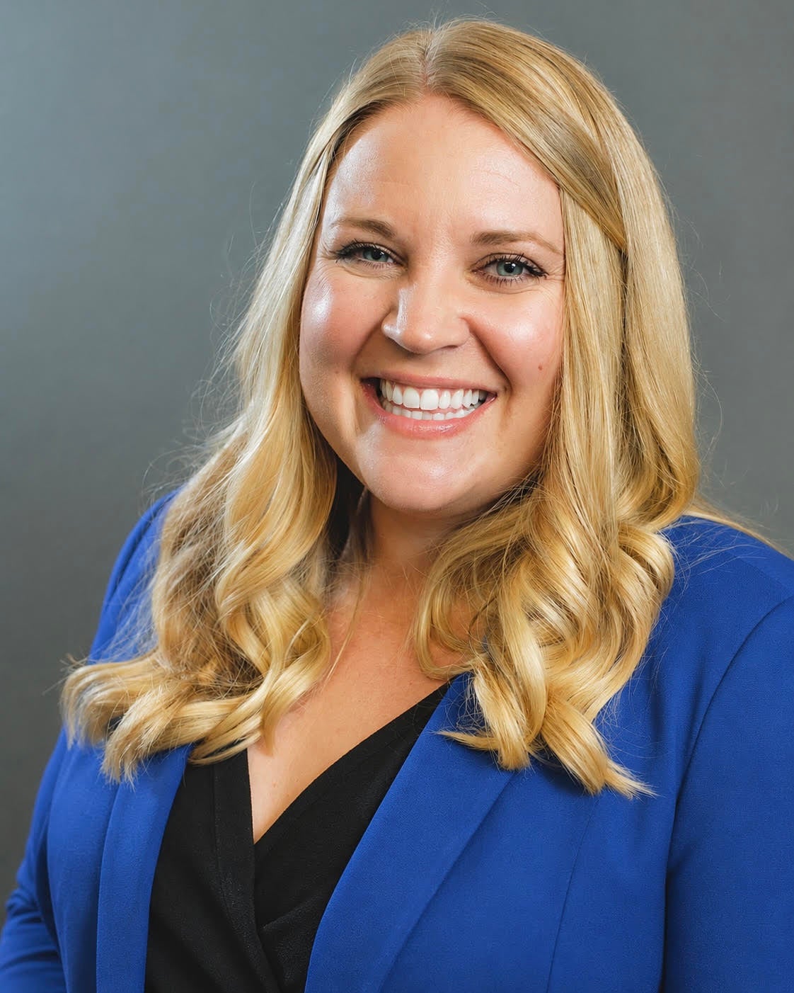 Portrait of Emilee Roberts smiling and wearing a blue blazer against a gray background.