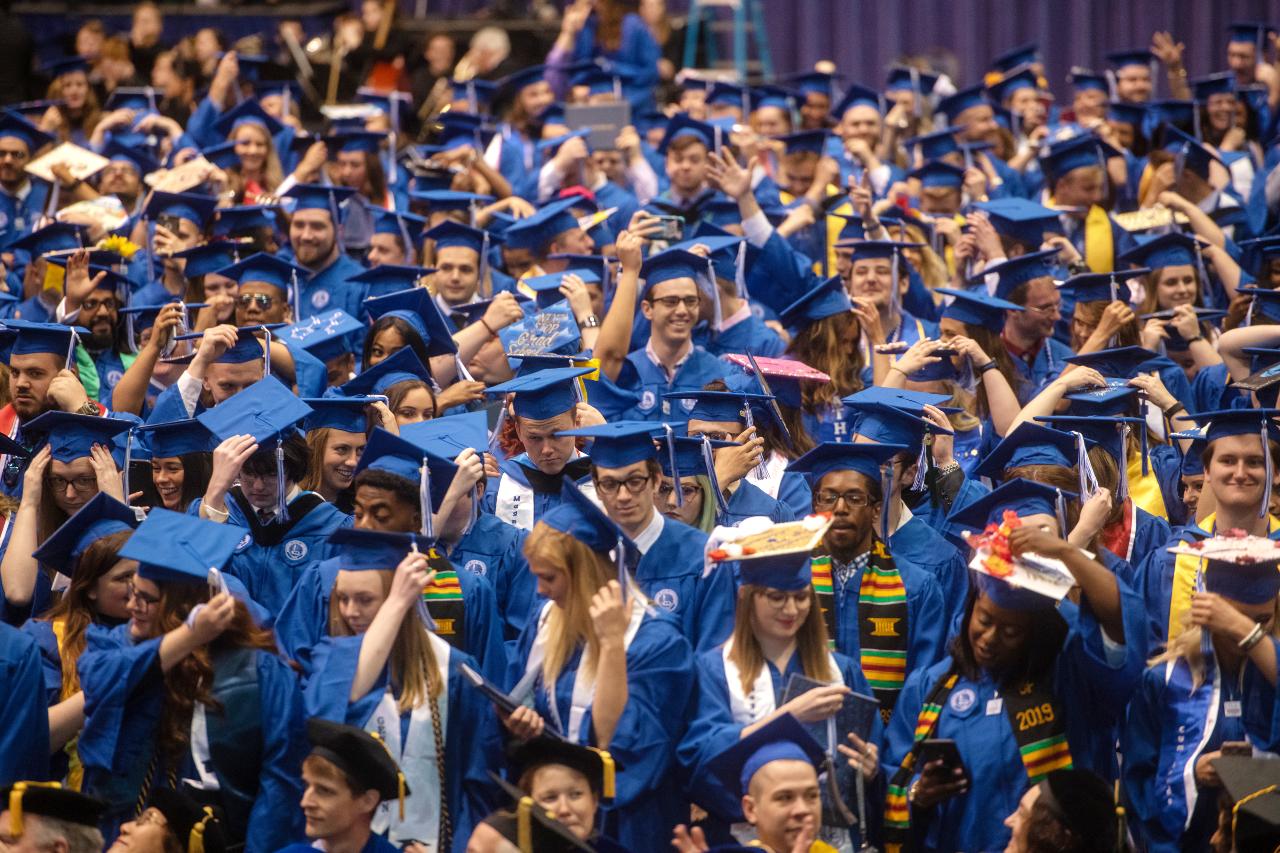 Large group of Indiana State University graduates in blue caps and gowns adjusting their caps and preparing during commencement ceremony.