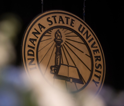 Seal of Indiana State University featuring a torch and an open book, with blurred foreground plants.
