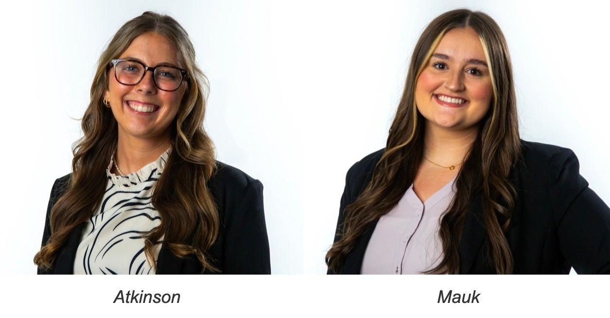Two young women with long hair smiling against a white background, both wearing blazers over light-colored tops.