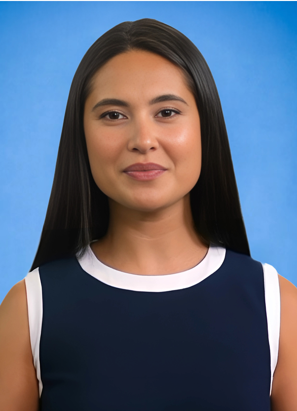 Young woman with long straight dark hair wearing a sleeveless navy dress with white trim, smiling slightly against a blue background.
