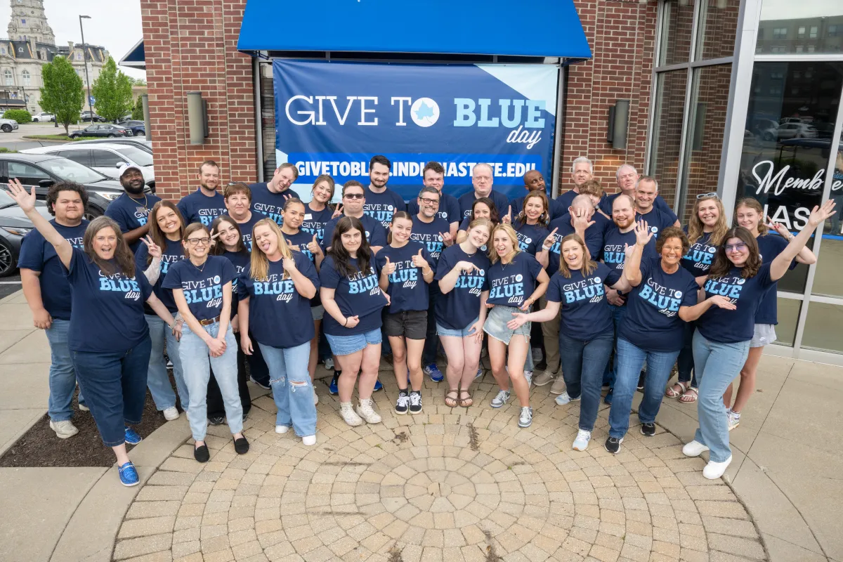 Indiana State University staff wearing Give to Blue Day shirts pose together outside a campus building.