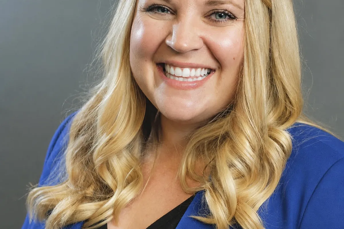 Portrait of Emilee Roberts smiling and wearing a blue blazer against a gray background.