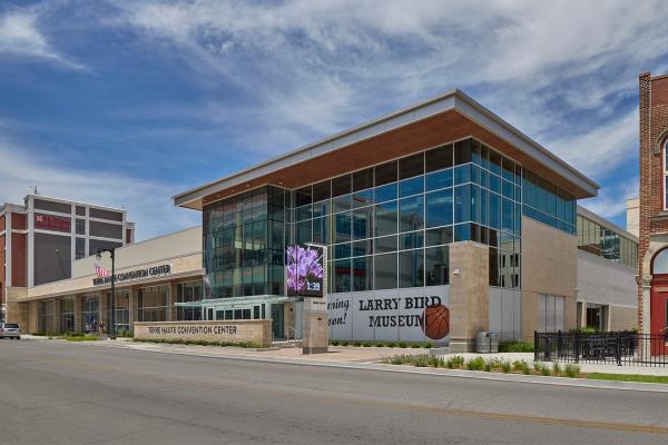 Exterior of the Terre Haute Convention Center with large glass windows, a sign for the upcoming Larry Bird Museum, and the Hilton Garden Inn in the background.