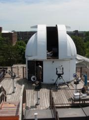 A large white observatory telescope sits atop a large wooden pier. Tools and equipment surround the structure.