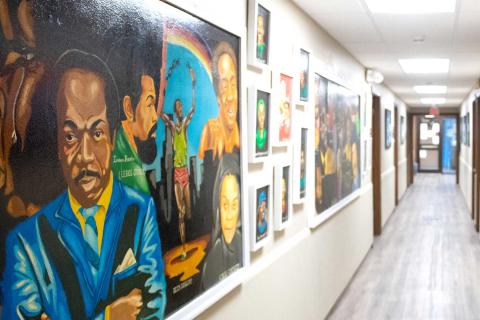 A hallway with a variety of picture frames on the wall. The frames feature colorful artwork of historic Black activists and known personalities.