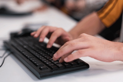 A detailed photo of a black laptop keyboard on a white table with two hands resting on the keyboard.