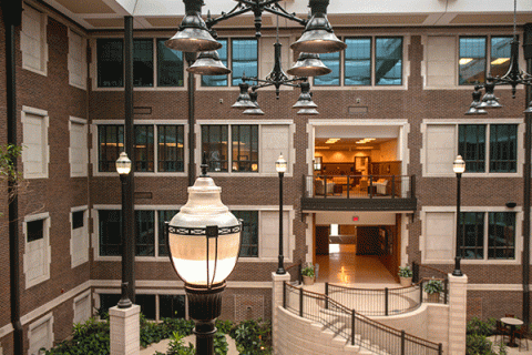Interior of an expansive atrium area in a brick, multi-story building with a large lamppost visible in the lower right corner and office windows and entryways arranged symmetrically on the far side. 