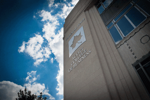 Exterior of a large building with a metallic Sycamore leaf logo and a sign reading “Federal Hall” above the logo and “Scott College of Business” below the logo with blue sky and clouds. 