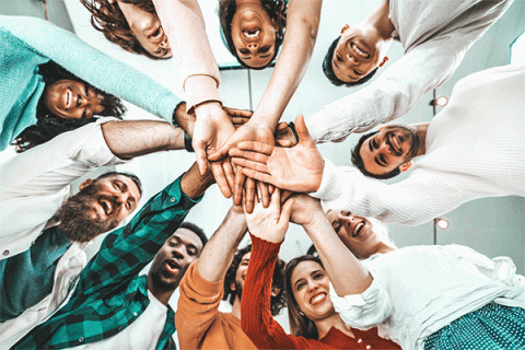 Multicultural group of people stacking hands together in a circle and looking down at the camera. 