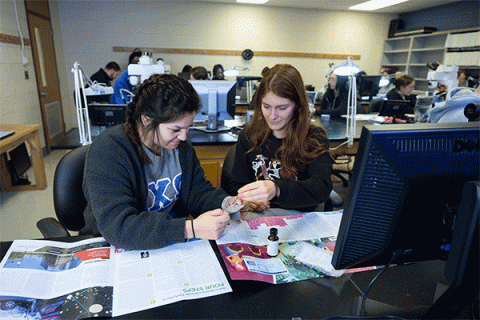 Two femal students working on at a desk in a lab analyzing fingerprints in the criminology class