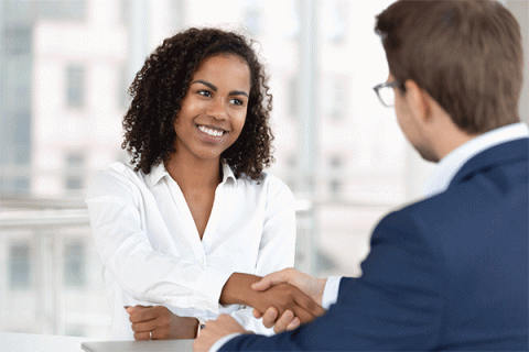 Smiling female human resources manager shakes the hand of a male job candidate whose back is turned to the camera.