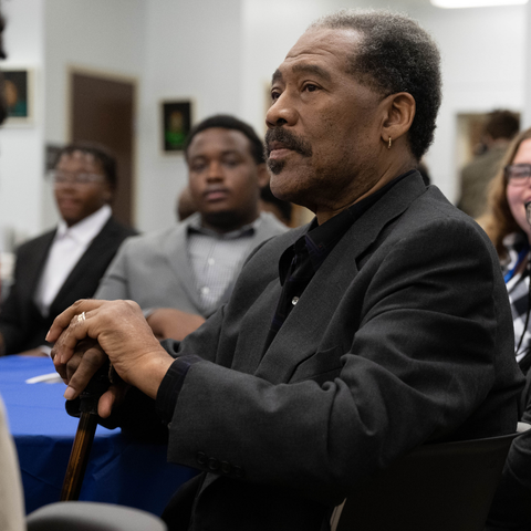 A distinguished gentleman with a cane listens attentively during a Black Alumni Networking event at Indiana State University, with other attendees in the background.